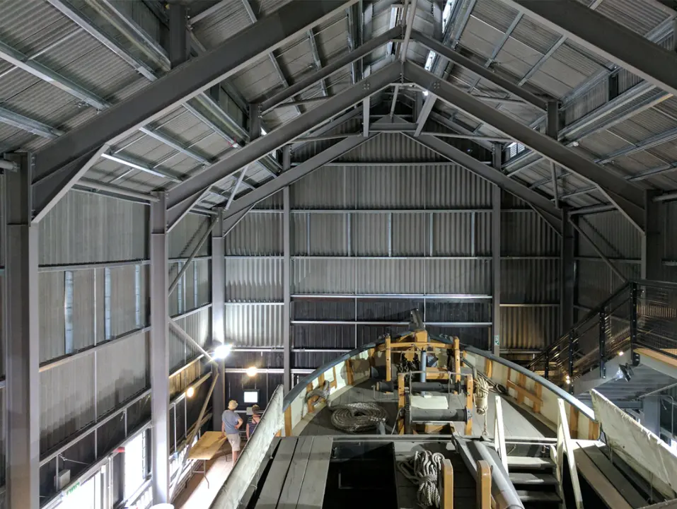 Interior of a steel-framed industrial building housing a large historic boat.